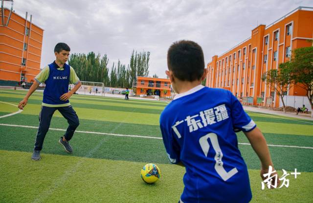 明德小学的学生在练习足球，球衣上写着“广东援疆”的字样。